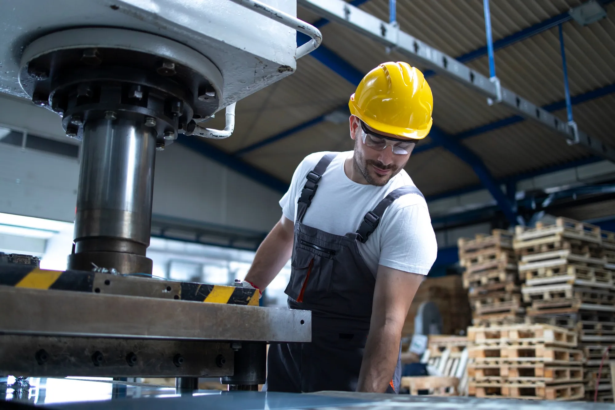 Worker in a hard hat operating a press on a plant floor