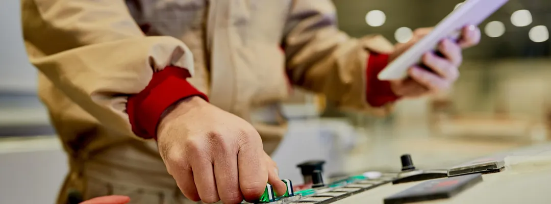 Operator checking a tablet while working controls on a panel