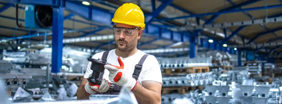 Operator in a hard hat inspecting a part among stacked castings