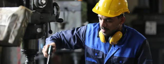 Operator in a hard hat working a tool at a drill press