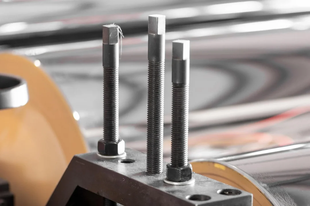 Three threaded bolts standing in a steel bracket, close up