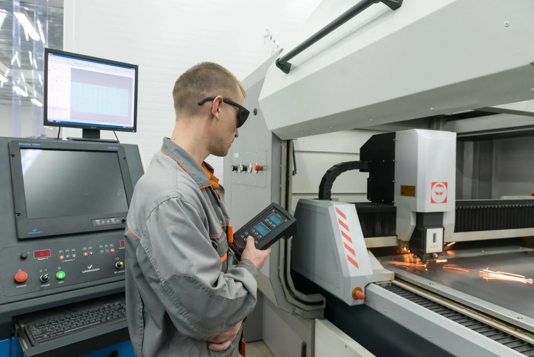 Operator at a CNC laser cutter, holding the handheld pendant while the head cuts sheet metal